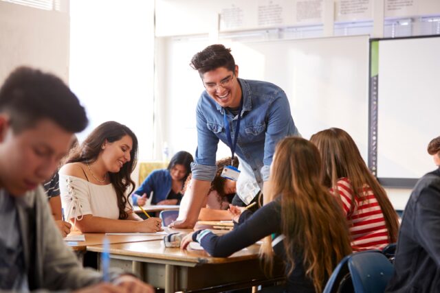 Teacher Standing By Student Table Teaching Lesson
