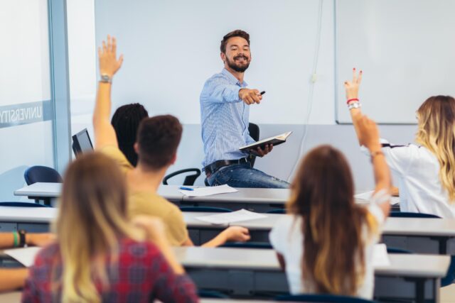 Group of students raising hands in class with teacher at front