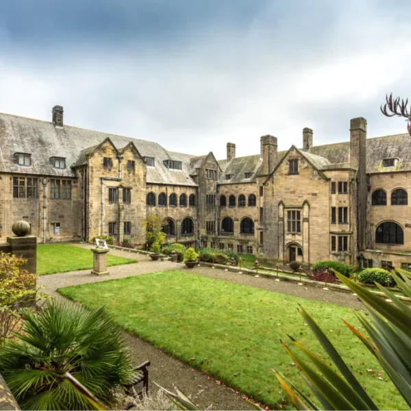 Historic courtyard and architecture at Bangor University, featuring stone buildings and landscaped gardens under a cloudy sky.