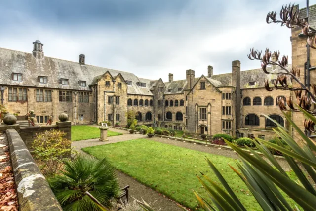 Historic courtyard and architecture at Bangor University, featuring stone buildings and landscaped gardens under a cloudy sky.